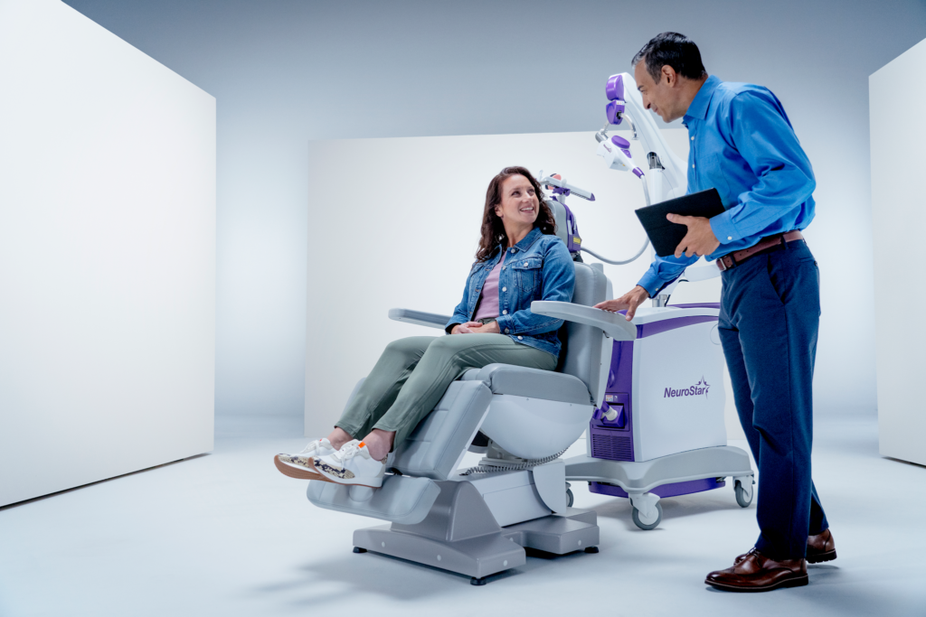 Provider explains NeuroStar treatment chair to smiling woman before session begins.