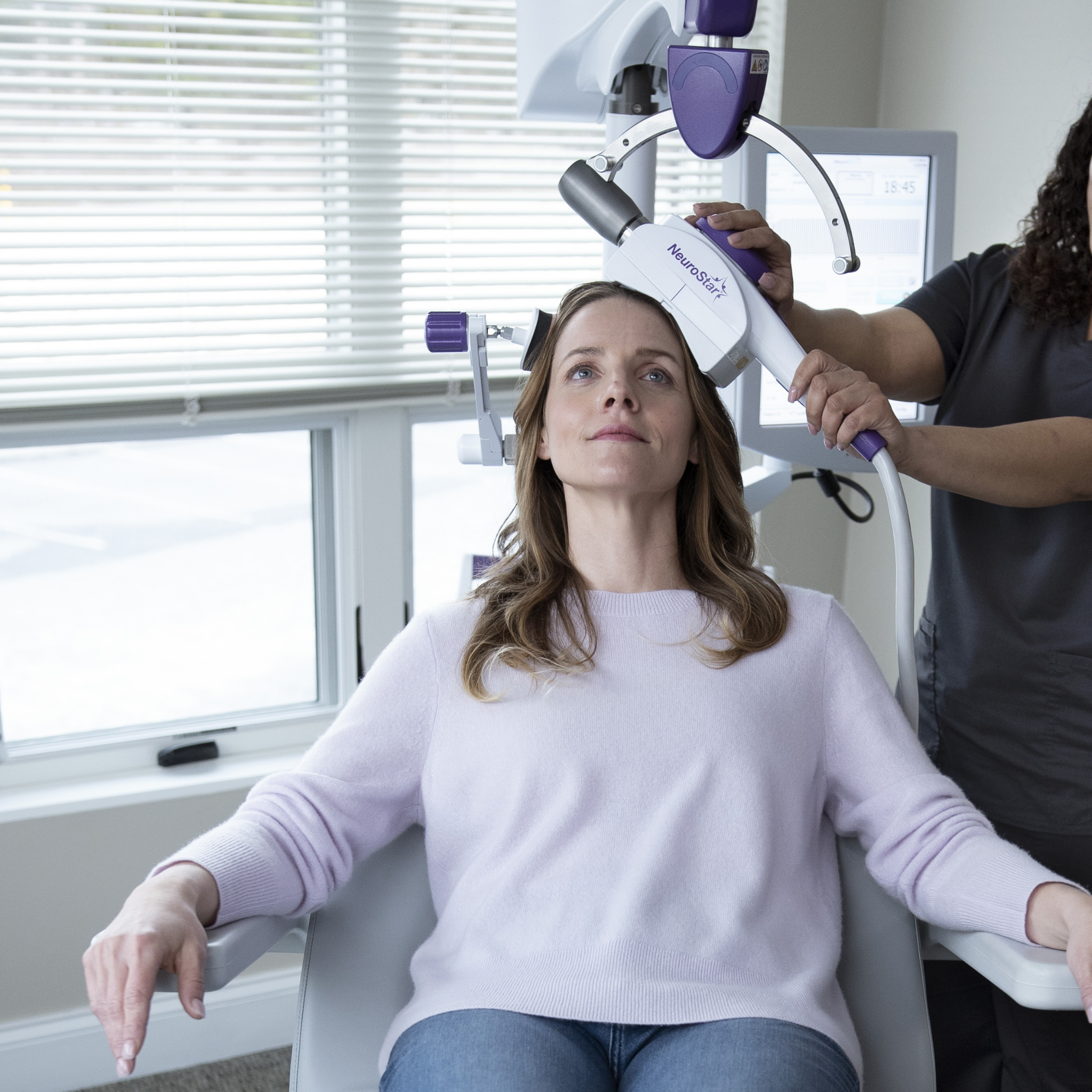 Can TMS Make You Feel Worse Before You Feel Better? 4 Woman receiving NeuroStar TMS therapy while seated in treatment chair, technician guiding device.